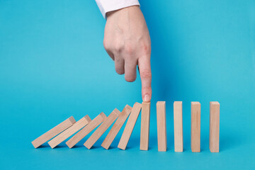 Woman stopping wooden blocks from falling on light blue background, closeup. Domino effect