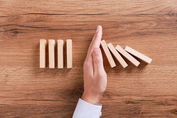 Man stopping wooden blocks from falling at table, top view. Domino effect