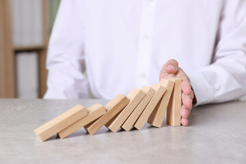 Man stopping wooden blocks from falling at table, closeup. Domino effect