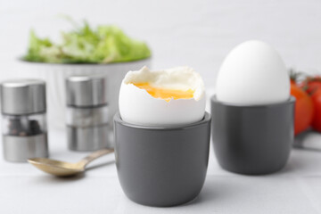 Soft boiled eggs in cups served on white table, closeup