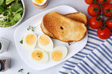 Hard boiled eggs with bread and tomatoes on light table, flat lay