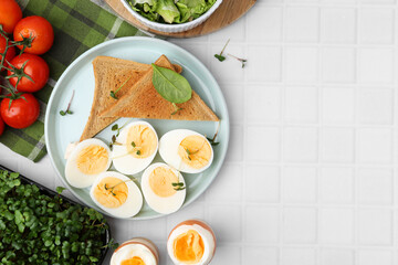 Cut hard boiled eggs with bread on white tiled table, flat lay. Space for text