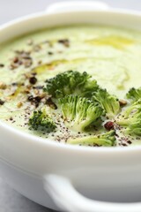 Delicious broccoli cream soup in bowl on light table, closeup