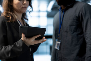 Teamworking colleagues in data center using tablet, analyzing metrics, optimizing storage volumes. Close up of server room workers using device, reviewing network paths, ensuring seamless operations