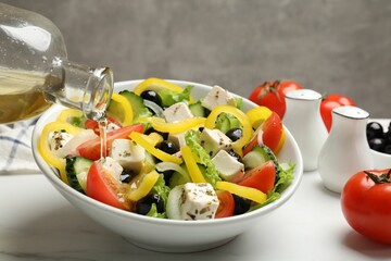 Adding olive oil to Greek salad at white marble table, closeup