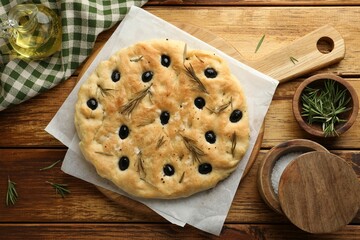 Delicious focaccia bread with olives, rosemary and salt on wooden table, flat lay