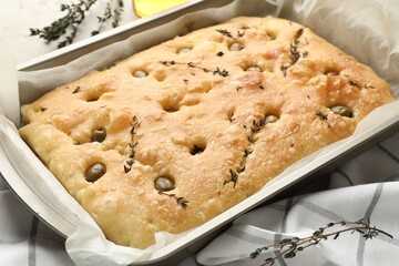 Delicious focaccia bread with olives and thyme in baking dish on table, closeup