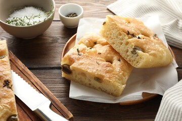 Pieces of delicious focaccia bread with olives, thyme, salt and knife on wooden table, closeup