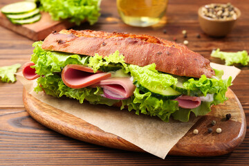 Delicious baguette sandwich with ham on wooden table, closeup