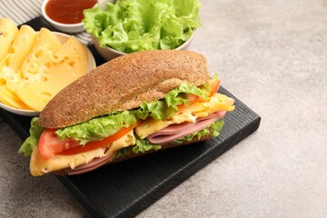 Delicious baguette sandwich with ham and ingredients on grey table