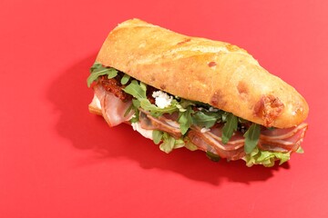 Baguette sandwich with ham and sun dried tomatoes on red background