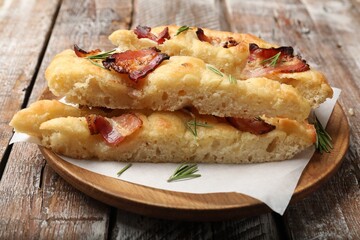 Slices of delicious focaccia bread with bacon and rosemary on wooden table, closeup