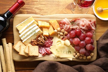 Different types of cut cheese and other snacks served with wine on wooden table, flat lay
