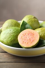 Fresh guava fruits in bowl on wooden table against blurred grey background, closeup