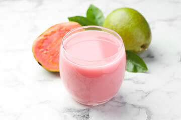Tasty guava juice in glass, leaves and fruits on white marble table, closeup