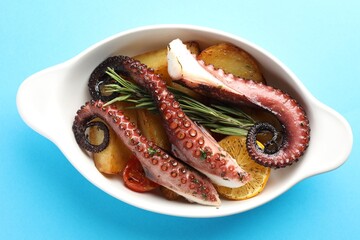 Fried octopus with vegetables, lemon and rosemary in baking dish on light blue background, top view © New Africa