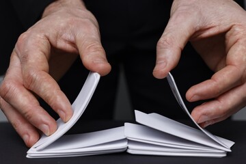 Illusionist shuffling playing cards at black table, closeup