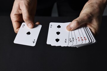 Illusionist shuffling playing cards on black background, closeup