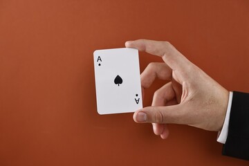 Illusionist showing playing card on dark orange background, closeup. Space for text