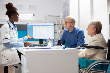 Elderly female wheelchair user and her husband speaking with african american doctor during medical...
