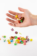 on white background in a small palm of the hand are pouring multi-colored caramels with different flavors and pictures children's favorite sweets risk of caries blood sugar excess weight