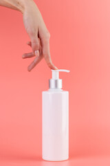 close-up on a soft pink background white glossy bottle with dispenser minimalist container for cosmetics beauty industry hermetic storage of liquids female hand presses the dispenser with a finger