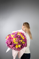 on light gray background a young blonde girl with a large bouquet of pink peony roses women's holiday March 8 first date the girl stands with her back turned away