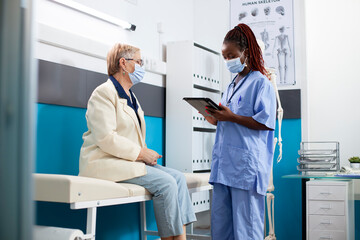 Fototapeta premium Nurse reviews medical results on tablet for caucasian elderly woman during consultation. Healthcare worker in uniform using digital device to update retired patient information for health checkup.