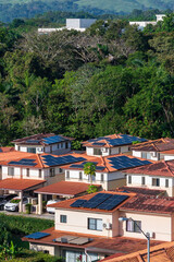 A suburban neighborhood with terracotta-roofed houses featuring solar panels, surrounded by lush...