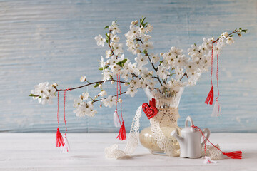 Blooming branches of cherry plum in a vase on the table and red and white symbols of Martenitsa on...