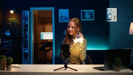 Gen Z girl in apartment studio using mobile phone to record, reviewing mini RGB lights. Young...