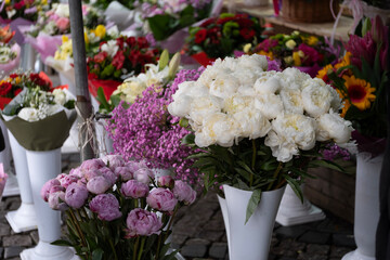 A colorful and abundant flower market scene with various floral arrangements, including pink and white peonies, purple flowers, and other vibrant blooms.
