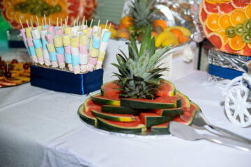 Fototapeta premium A table with a chocolate fountain and various colorful fruits ready to eat with a green led light and a swan shape made of fruit pieces