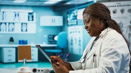 African american specialist reviewing data and records in her office, working on improving healthcare services at the treatment center. Healthcare provider works in a private clinic. Camera B.