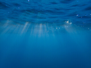Dark blue ocean surface seen from underwater. Abstract waves underwater and rays of sunlight...