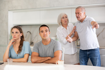 Obraz premium Portrait of an offended married couple in a home kitchen, which mature family members reprimand. Family conflict