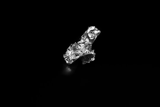 A ball of aluminum foil on a black table against a black backdrop