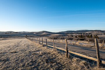 Fototapeta premium A frosty morning reveals a rural landscape a road winding through fields bordered by a rustic wooden fence