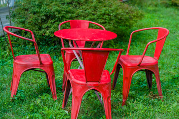 Fototapeta premium A set of four red metal chairs around a matching table on a grassy lawn.