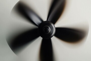 Abstract view of a spinning ceiling fan with blurred motion, showcasing a sleek black design against a neutral background, evoking a sense of coolness and comfort