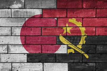 colourful painted big flag of japan and flag of angola on a massive old brick wall background....