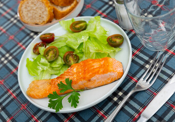 mediterranean cuisine.board table in plate narrow slice of fried salmon with green salad and cherry tomatoes, white bread