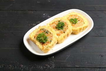 Rolled omelette slices filled with mixed vegetables and herbs, beautifully plated with parsley garnish, traditional Asian style savory snack or appetizer on dark background.