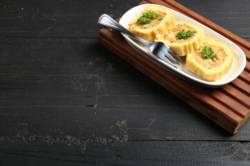 Traditional cake from Indonesia called Sus Brood, like Korean Egg Roll, with white plate, fork, and wood, isolated with dark wood background	