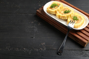 Traditional cake from Indonesia called Sus Brood, like Korean Egg Roll, with white plate, fork, and wood, isolated with dark wood background