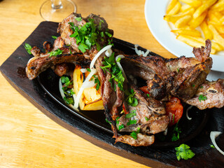 Appetizing grilled mutton ribs served on black plate with potatoes and baked bell pepper