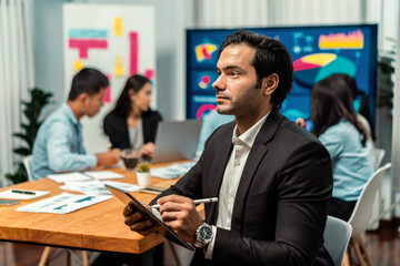 Portrait of businessman or analyst looking at camera with his colleague analyzing data analysis in dynamic business strategy investment planning meeting. Meticulous