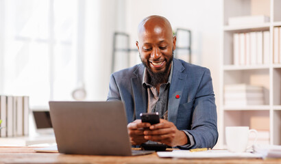 Fototapeta premium African American Businessman using mobile phone while working with laptop at workplace office. browsing site on cellphone.