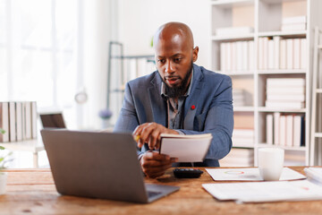 An office scene showing a professional at his desk, using a laptop for various business activities and strategies.African American Businessman work.