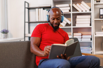 Cropped shot of a happy senior African American man sitting alone and listening to music through headphones while reading a book.